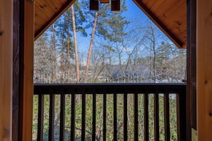 Une terrasse en bois dotée d’une rambarde, offrant une vue sur une zone boisée avec de grands arbres et un ciel dégagé.