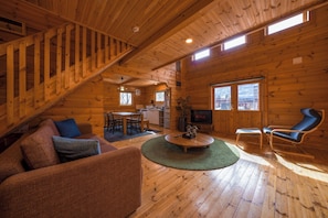 L’intérieur d’un chalet en bois comprend un escalier, un salon, un coin repas, une cuisine et de grandes fenêtres.