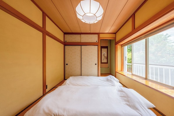A traditional Japanese-style room with tatami flooring, a low ceiling, and a sliding door leading to another room.