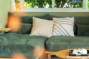 A green sofa with a beige pillow and striped pillow, a small wooden side table, and a round coffee table with a teapot and tray.