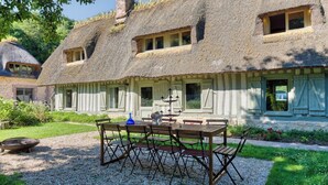 Ein traditionelles Haus mit einem Reetdach, einer Kiesterrasse, Holzmöbeln und einem kleinen Garten.