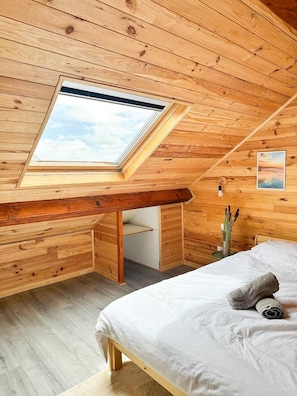 Ein Schlafzimmer mit Oberlicht, Holzwänden, einem Bett und einem Nachttisch.