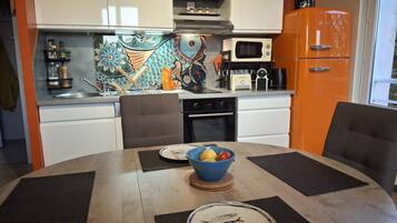 A modern kitchen with white cabinets, a microwave, a coffee maker, and a vintage orange refrigerator.