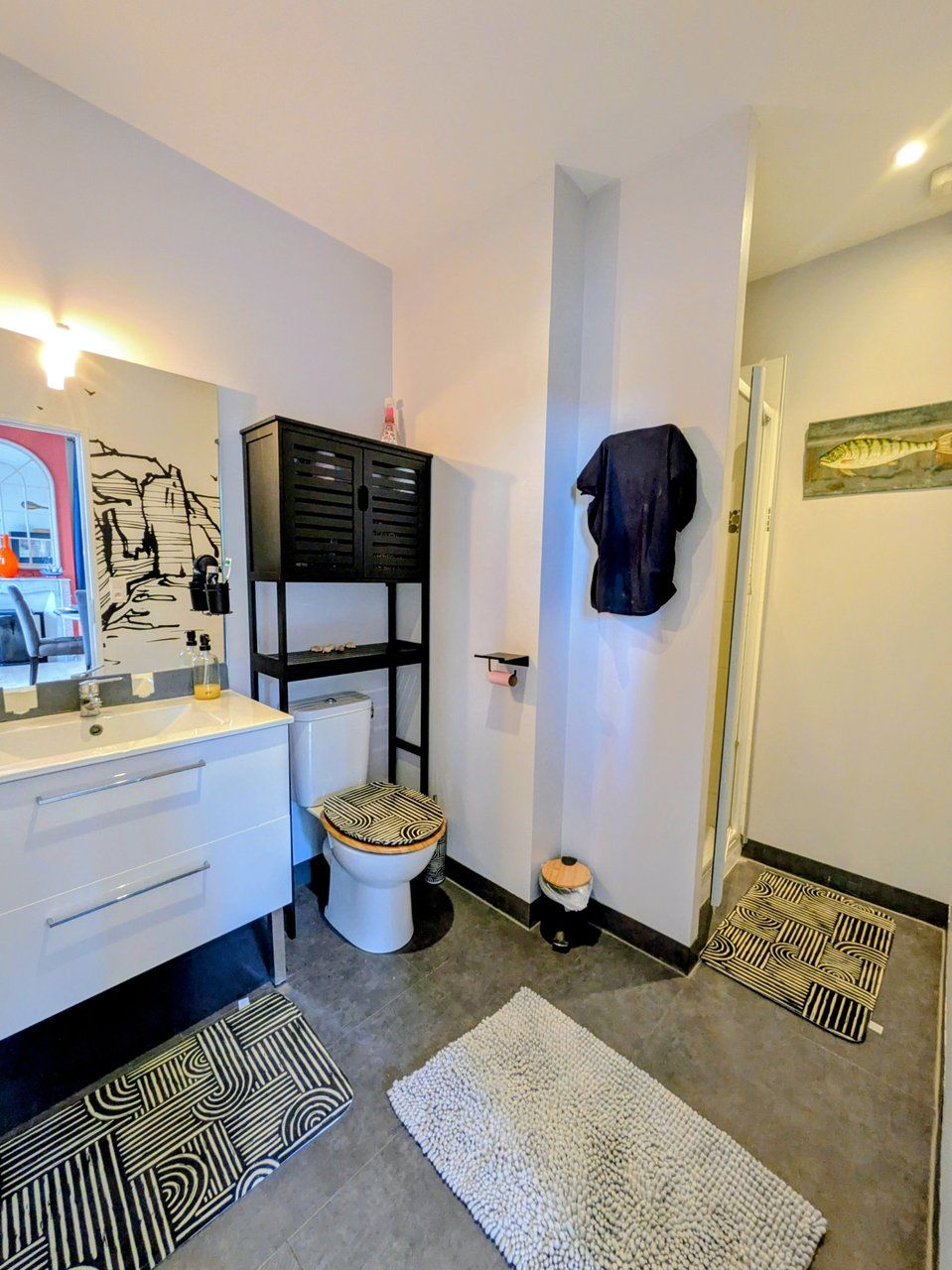 A modern bathroom with a white sink, black cabinets, a toilet, and a shower area.