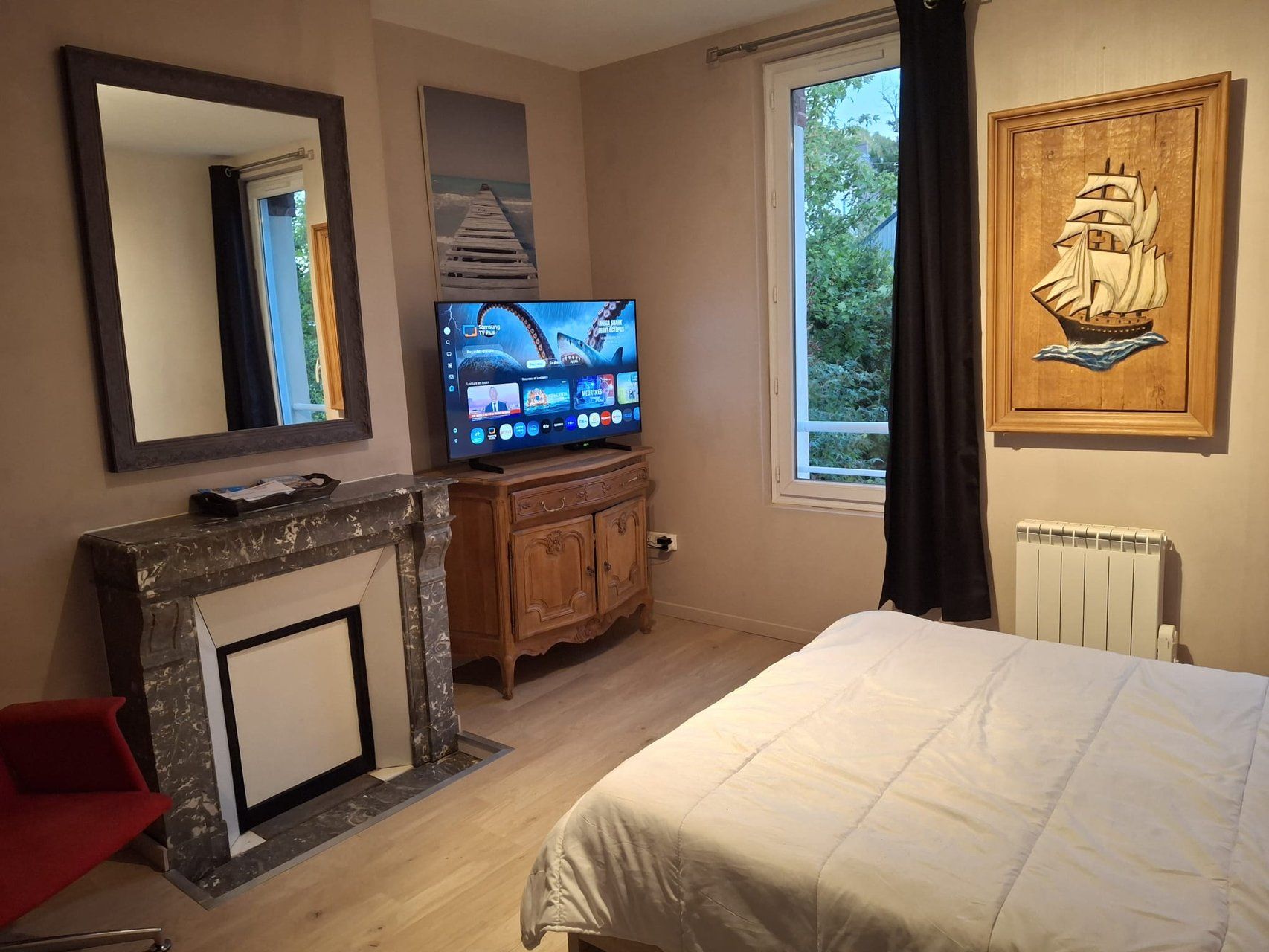 Une chambre à coucher comprenant un lit, un téléviseur, une cheminée, une fenêtre avec vue et une œuvre d’art accrochée au mur.