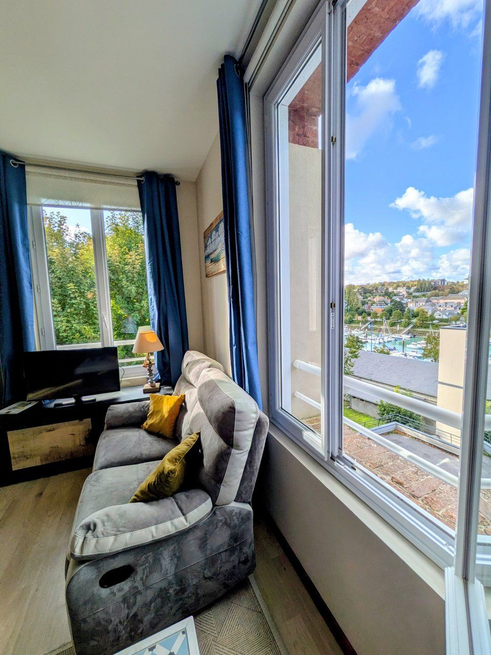 A living room with a sofa, a TV, and a view of a town through a large window.