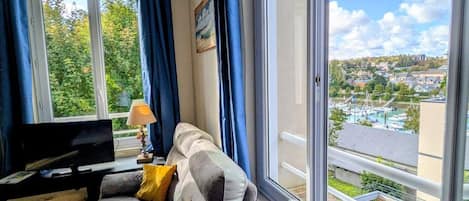 Una sala de estar con un sofá, un televisor y vistas a un pueblo a través de un ventanal amplio.