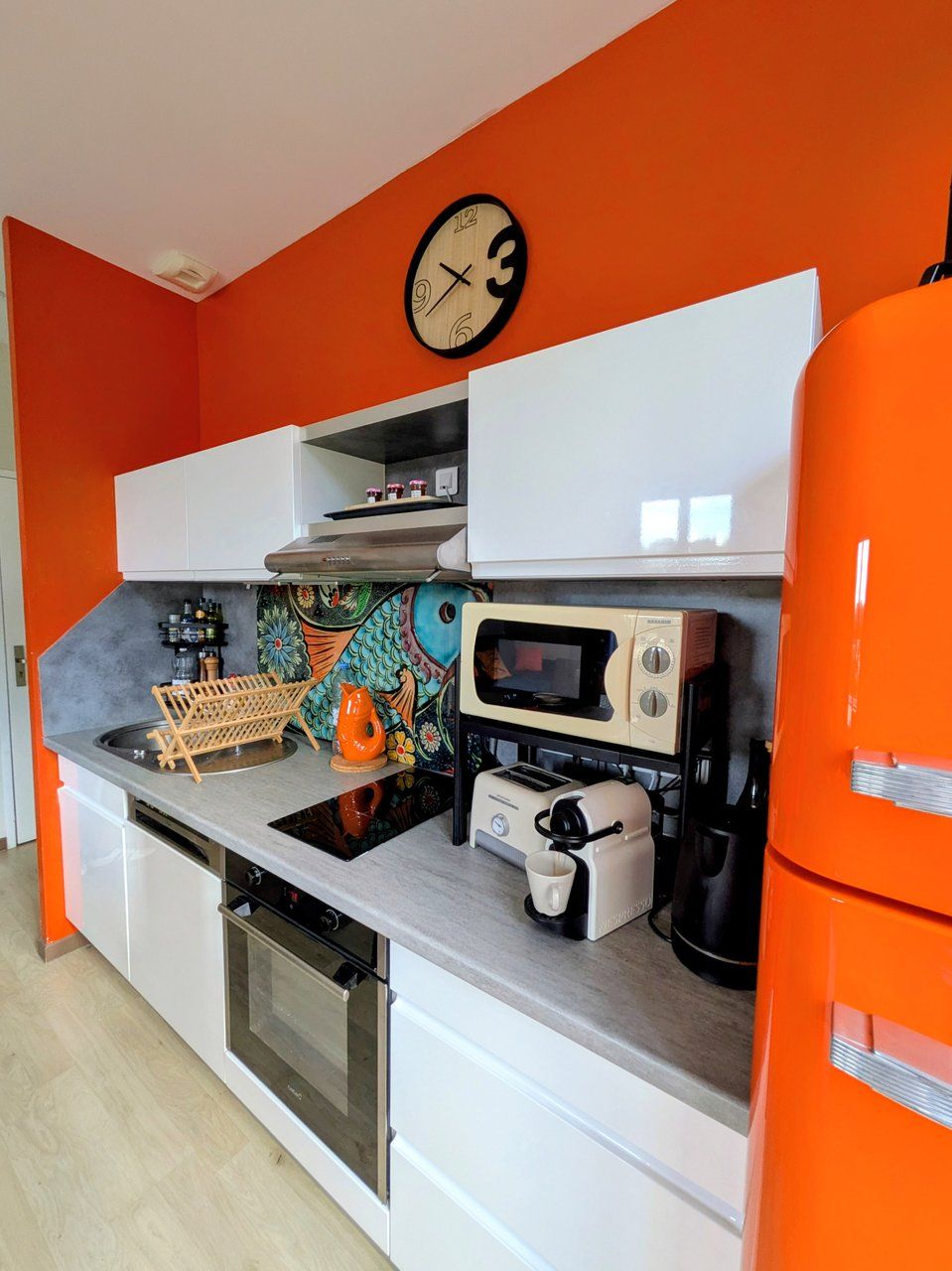 Una cocina con microondas, tostadora y cafetera sobre la encimera, y un reloj en la pared.