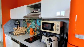 Una cocina con microondas, tostadora y cafetera sobre la encimera, y un reloj en la pared.