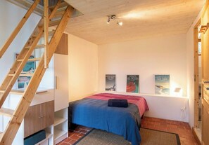 Ein Schlafzimmer mit einer Holztreppe, einem Bett mit blauer Bettdecke und zwei Bildern an der Wand.