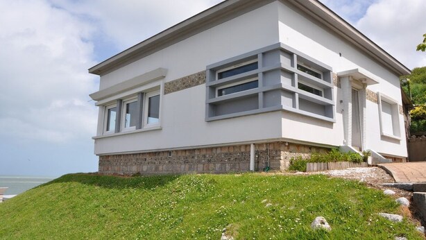 A modern two-story house with a flat roof, large windows, and a stone foundation.