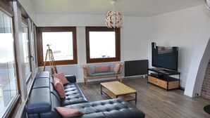 A modern living room with a black leather sofa, a wooden coffee table, and a television on a wooden stand.