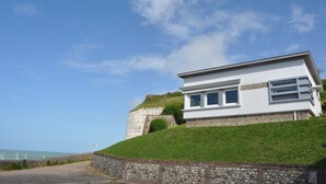 Un edificio moderno con fachada blanca y base de piedra, situado en una colina cubierta de césped con vistas al mar.