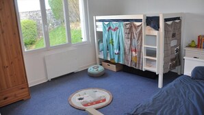 A child's bedroom with bunk beds, a wooden wardrobe, a desk, and a window with a view of greenery.