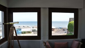 Una habitación con telescopio, ventanas amplias y vista al mar y edificios.