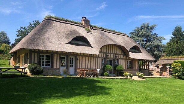 A traditional house with a thatched roof, a front porch, and a well-maintained lawn.