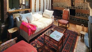 Ein gemütliches Wohnzimmer mit freiliegenden Holzbalken, einem Kamin aus Ziegelsteinen und einer komfortablen Sitzecke mit Sofa und Sesseln.