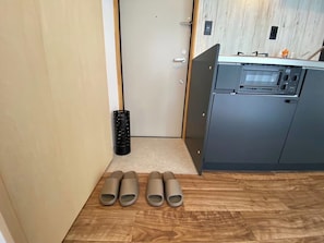 Una pequeña cocina con microondas, un lavamanos y una puerta. Hay cuatro objetos cilíndricos en el suelo.