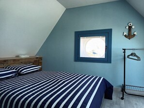 Une chambre à coucher avec un lit, une tête de lit en bois, une fenêtre donnant sur un beau paysage et un porte-manteau fixé au mur.