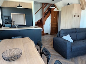 Una cocina moderna con microondas integrado, una mesa de comedor de madera con sillas, un sofá azul oscuro y una escalera que lleva a otro nivel.