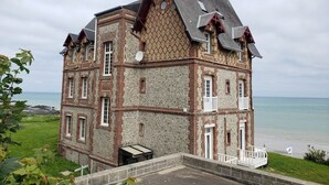 A large, multi-story building with a brick facade, a balcony, and a view of the sea. - Apartment with superb sea and land views (Veulettes-sur-Mer)