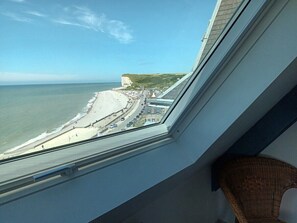 Vista desde una ventana sobre una playa, con una carretera y edificios a lo lejos.