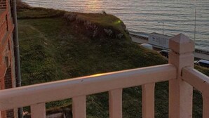 A sunset view from a balcony overlooking a body of water, with a grassy area and a brick building to the left. - Apartment with superb sea and land views (Veulettes-sur-Mer)