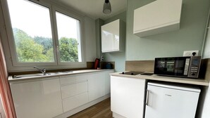 A compact kitchen with a built-in microwave, a small refrigerator, and a window providing a view of greenery outside. - Roirand | Romantic Beach on Foot (Veules-les-Roses)