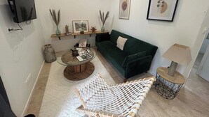 Un salon avec un canapé vert, une table basse ronde, un hamac blanc, une lampe et un téléviseur fixé au mur.