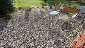 Une terrasse avec un sol en gravier, deux tables rondes et deux chaises en osier.