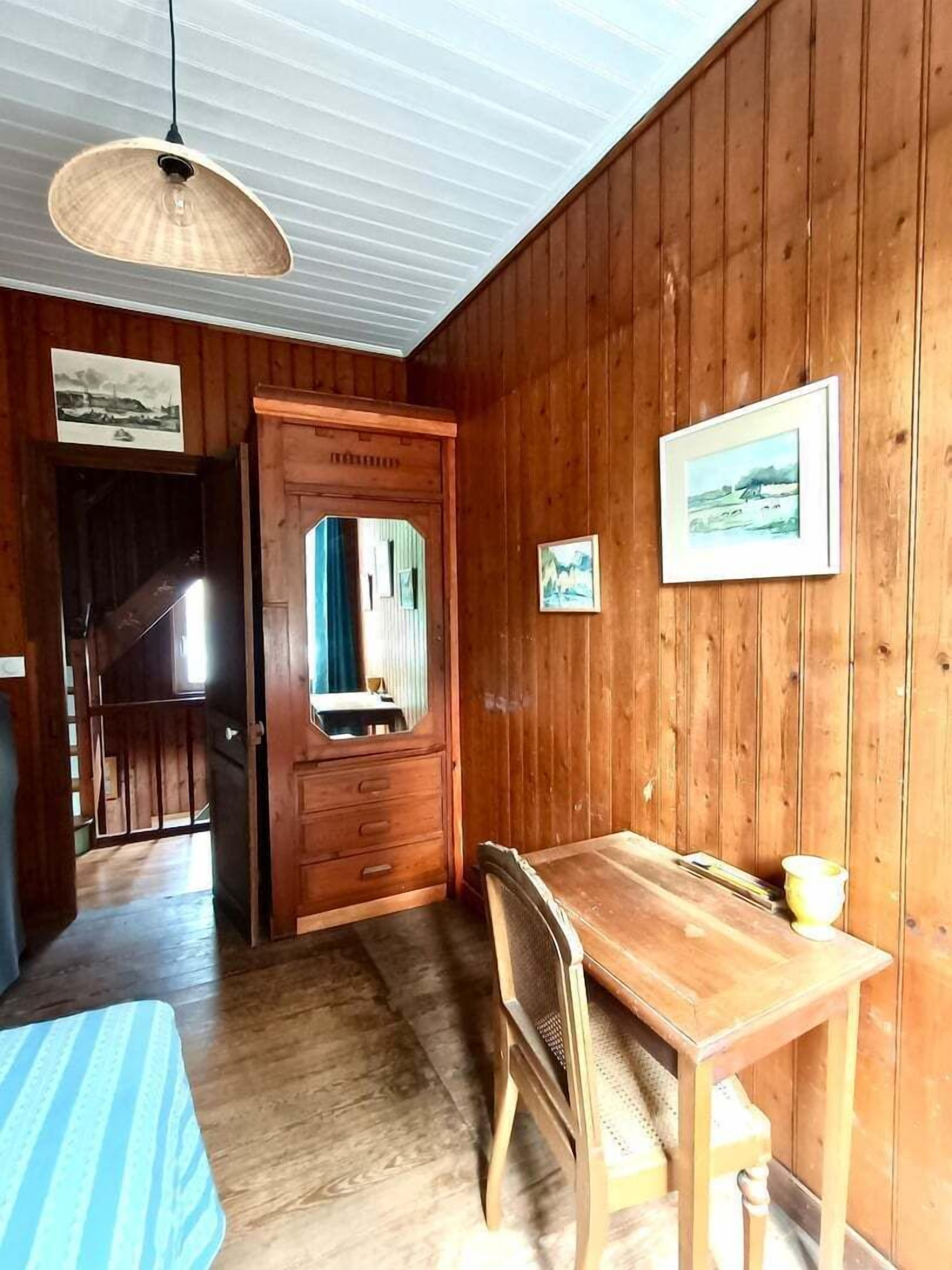 Habitació amb panells de fusta, taula de dinar, cadira, llum penjant i porta cap a una altra habitació.