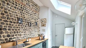 Une cuisine moderne avec un mur de pierres apparentes derrière l’évier, une verrière et une table à manger en bois.