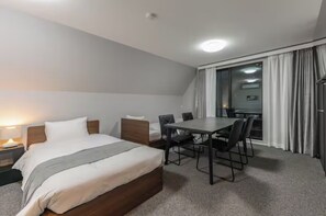 Ein Hotelzimmer mit Bett, Nachttisch, Lampe und Esstisch mit Stühlen.