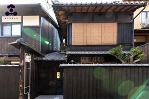 Una casa tradicional japonesa de madera con suelo de esteras de tatami, un portón de madera oscura y un pequeño árbol creciendo en el tejado.