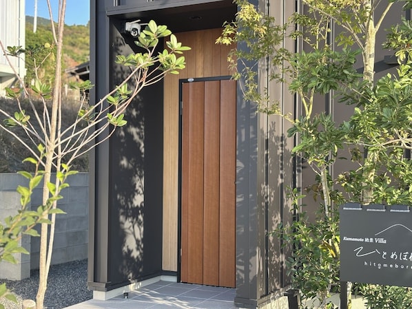 A modern villa entrance with a wooden door, a security camera, and a signboard.