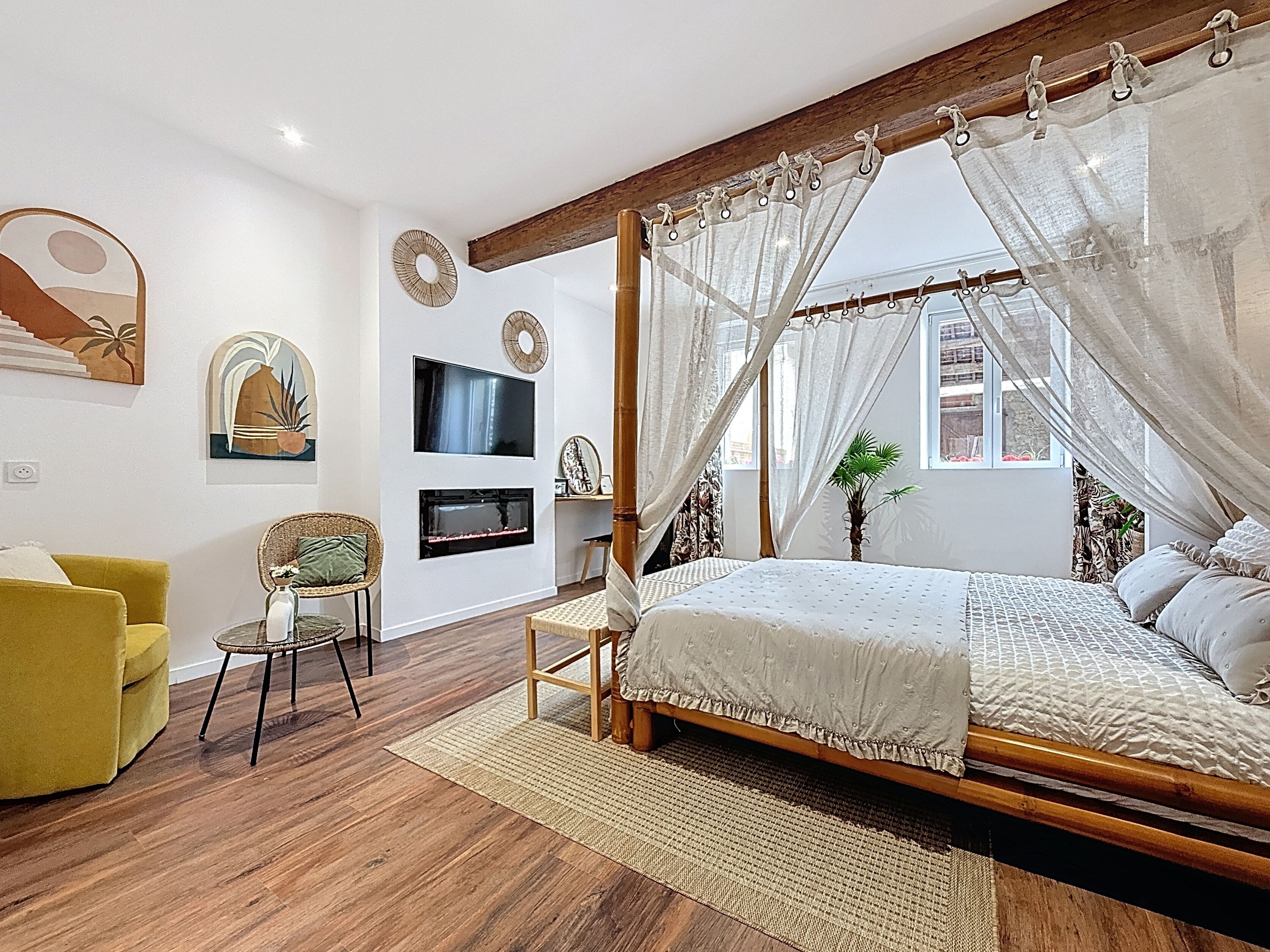A bedroom with a four-poster canopy bed, a television mounted on the wall, and a small table with a chair.