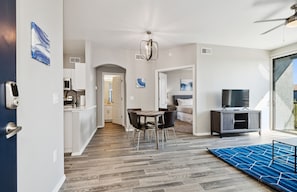 A modern living room with a dining area, a TV, and a large window. - Pure Suites Ascent 1 Bed Gym Pool (Phoenix)