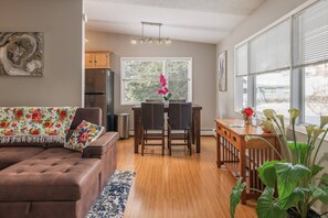 A modern living room with a sofa, dining table, chairs, and a kitchen area with cabinets and a refrigerator. - Entire Duplex! Downtown 4 Bdr - King beds (Anchorage)