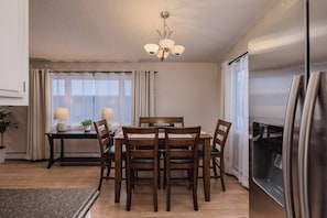 A dining area with a wooden table and chairs, a chandelier, and a refrigerator. - Entire Duplex! Downtown 4 Bdr - King beds (Anchorage)