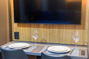 Uma área de jantar com uma mesa posta para dois, uma televisão de tela plana na parede e um controle remoto sobre a mesa.