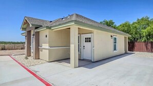 A single-story building with a flat roof, beige exterior walls, and a small attached garage. - Enjoyable 2-bedroom house with AC  1min from Kickapoo Lucky Eagle Casino. (Eagle Pass)