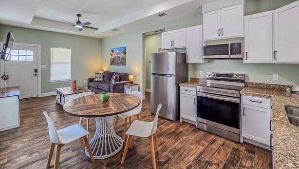 A modern kitchen with white cabinets, stainless steel appliances, and a wooden dining table with chairs. - Enjoyable 2-bedroom house with AC  1min from Kickapoo Lucky Eagle Casino. (Eagle Pass)
