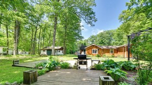 Eine Holzterrasse führt zu einem Haus mit Grillplatz, umgeben von üppigem Grün und Bäumen.