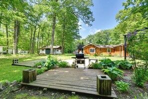 A wooden deck leading to a house with a barbecue area, surrounded by lush greenery and trees.