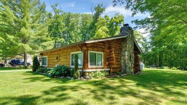 Eine Blockhütte mit einem Steinkamin, einer Veranda und einem gepflegten Rasen.