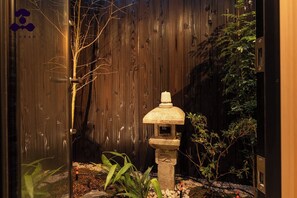 Ein Steinkandelaber in einem Garten mit Holzpforte und verschiedenen Pflanzen.