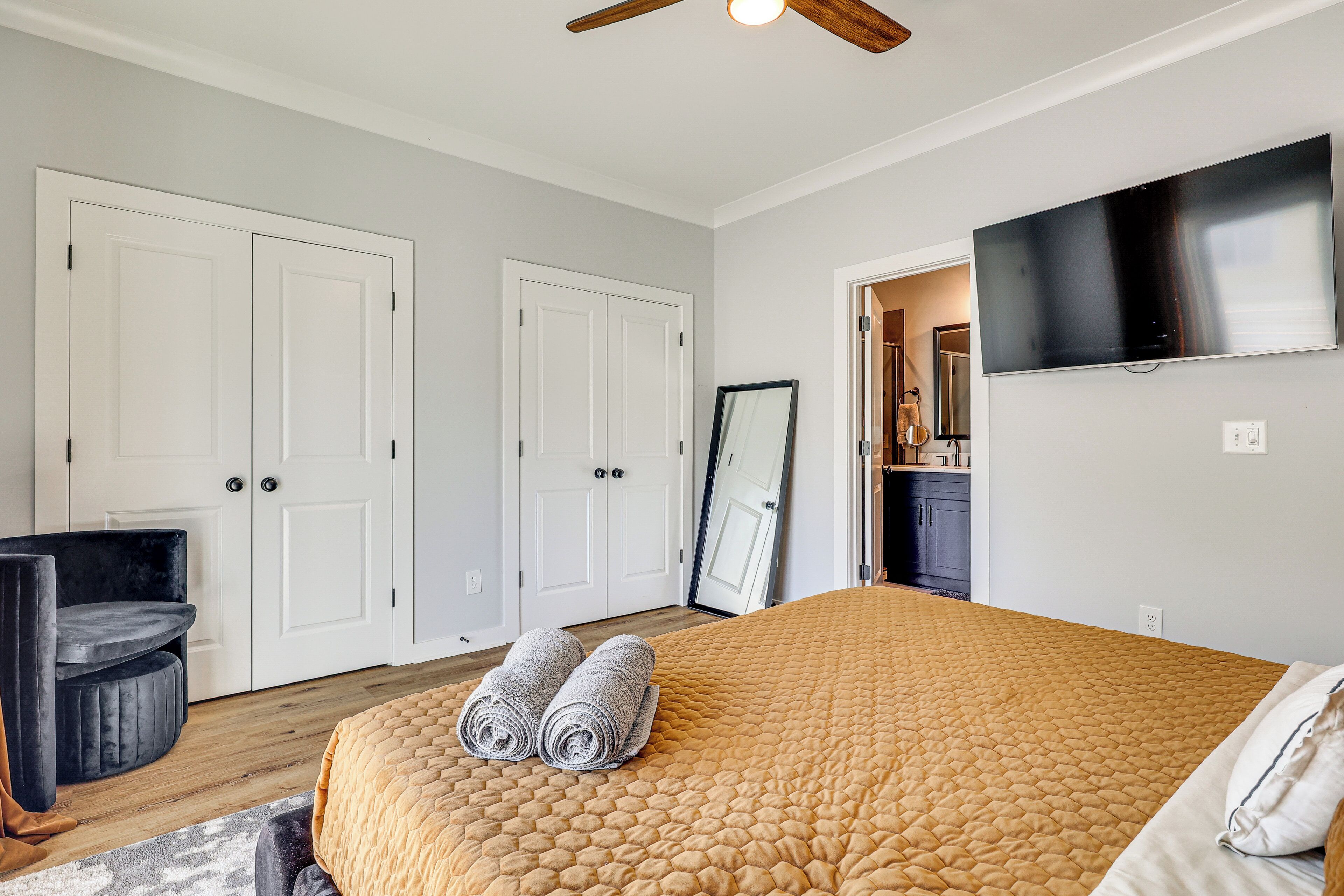 A bedroom with a large bed, a ceiling fan, a flat-screen TV, and a wardrobe.