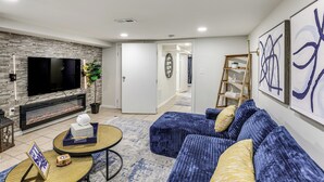 A modern living room with a fireplace, a large flat-screen TV, a blue sofa, and a coffee table. - Walk to Patterson Park! Pet-Friendly Townhome (Baltimore)