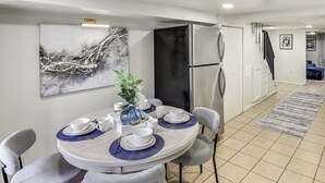 A modern kitchen with a dining area, featuring a stainless steel refrigerator, a round dining table with blue placemats, and grey upholstered chairs. - Walk to Patterson Park! Pet-Friendly Townhome (Baltimore)