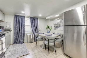 A modern kitchen with a stainless steel refrigerator, white cabinets, a dining table with chairs, and a patterned rug. - Walk to Patterson Park! Pet-Friendly Townhome (Baltimore)